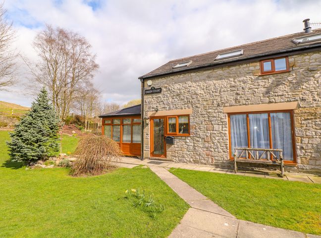 A stone house with wooden framed windows doors and a garden with a bench at Monks Cottage in Buxton
