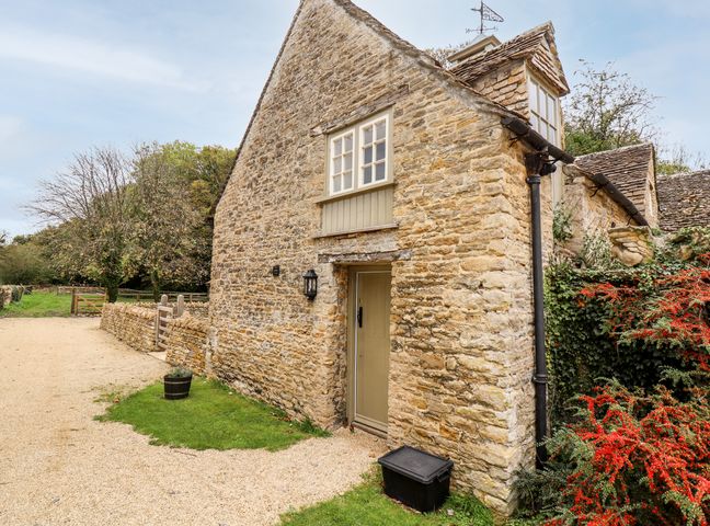 A stone cottage with a gravel pathway a wooden door a window vines and red berries at The Clock Tower in South Cerney