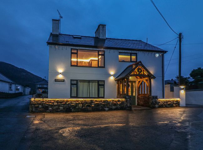 A two-story house with lit porch and exterior lights at night at Murmur Y Mor in Nefyn