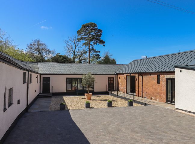 A courtyard with gravel area and potted tree surrounded by white and brick buildings at Lower Marsh Barns in Ottery St Mary