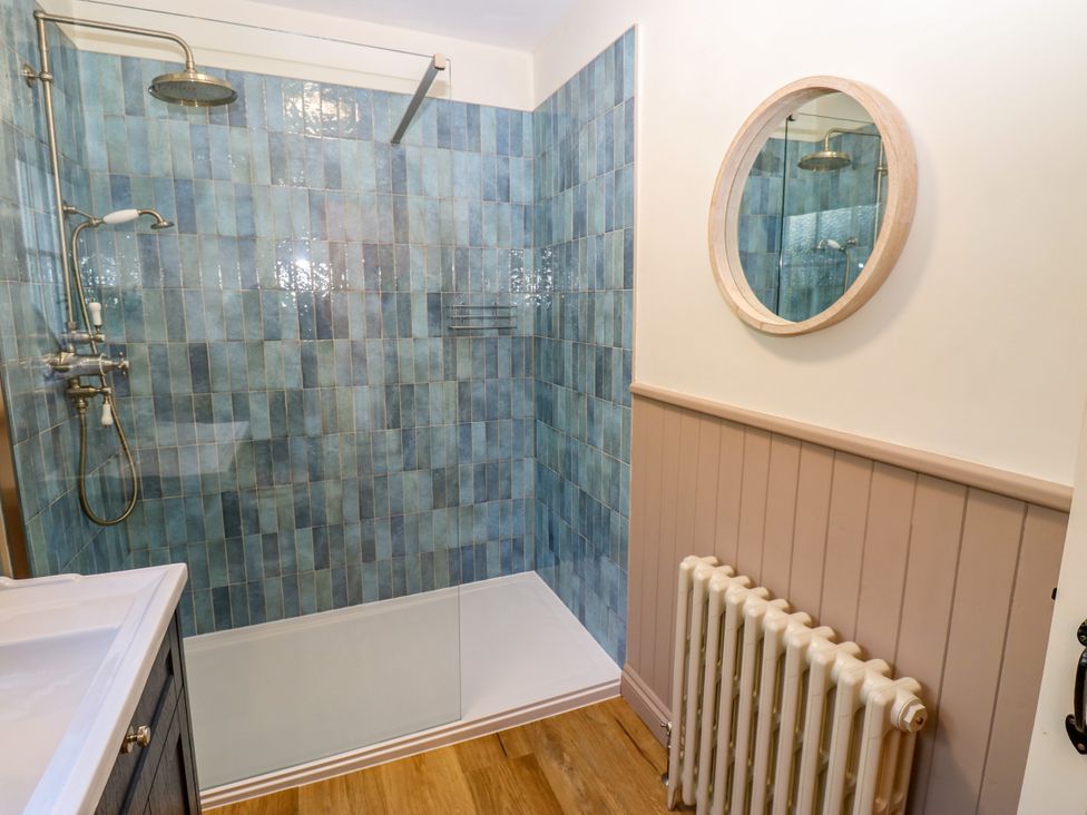 A shower area with blue tiles and a mirror at Old Workhouse Cottage in Stanhope