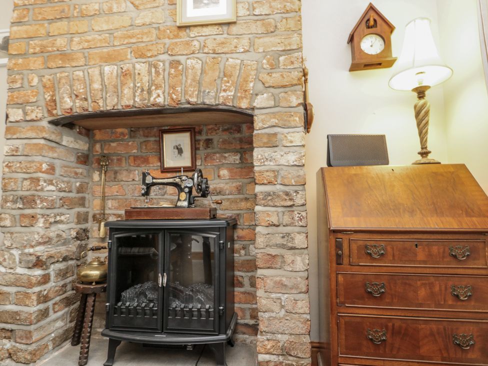 A fireplace with a sewing machine beside a wooden cabinet at Chapel Cottage in Filey