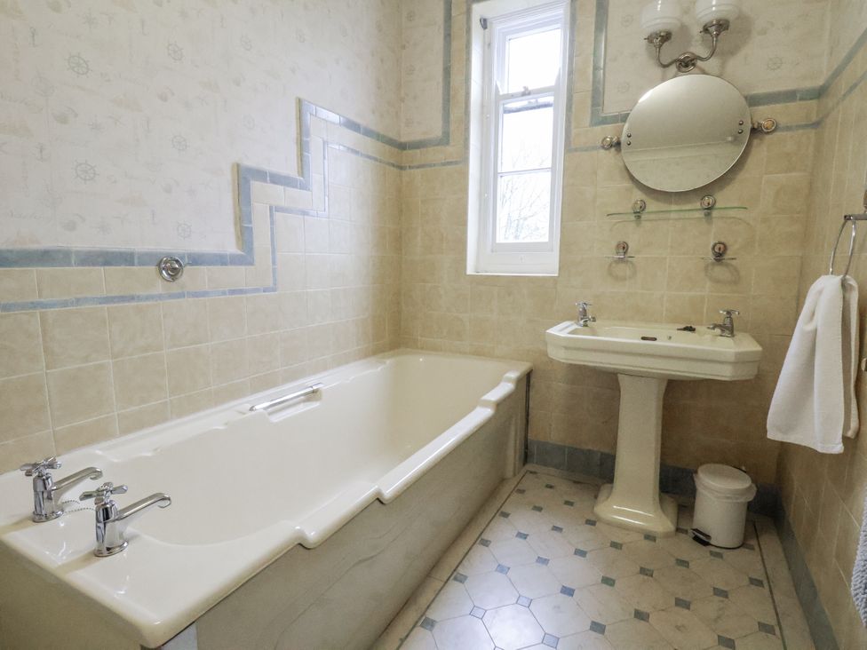 A bathroom with a bathtub, sink, and mirror at The Manor House in Scarborough