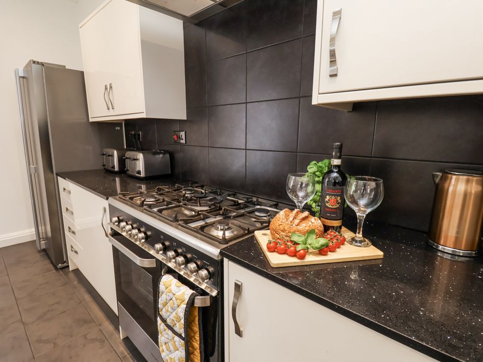 A kitchen with a gas stove, refrigerator, and wine on a counter at Tennyson House in Scarborough