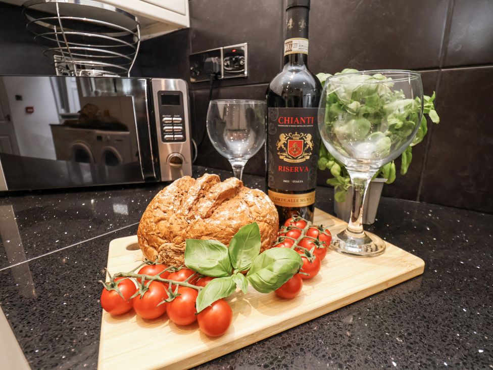 A kitchen counter with wine, bread, tomatoes, and glasses at Tennyson House Scarborough