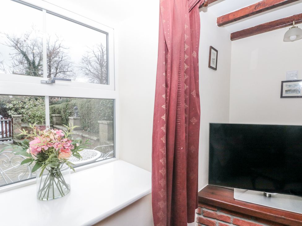 A living room with a window displaying flowers and a television at Dove Cottage in Sleights