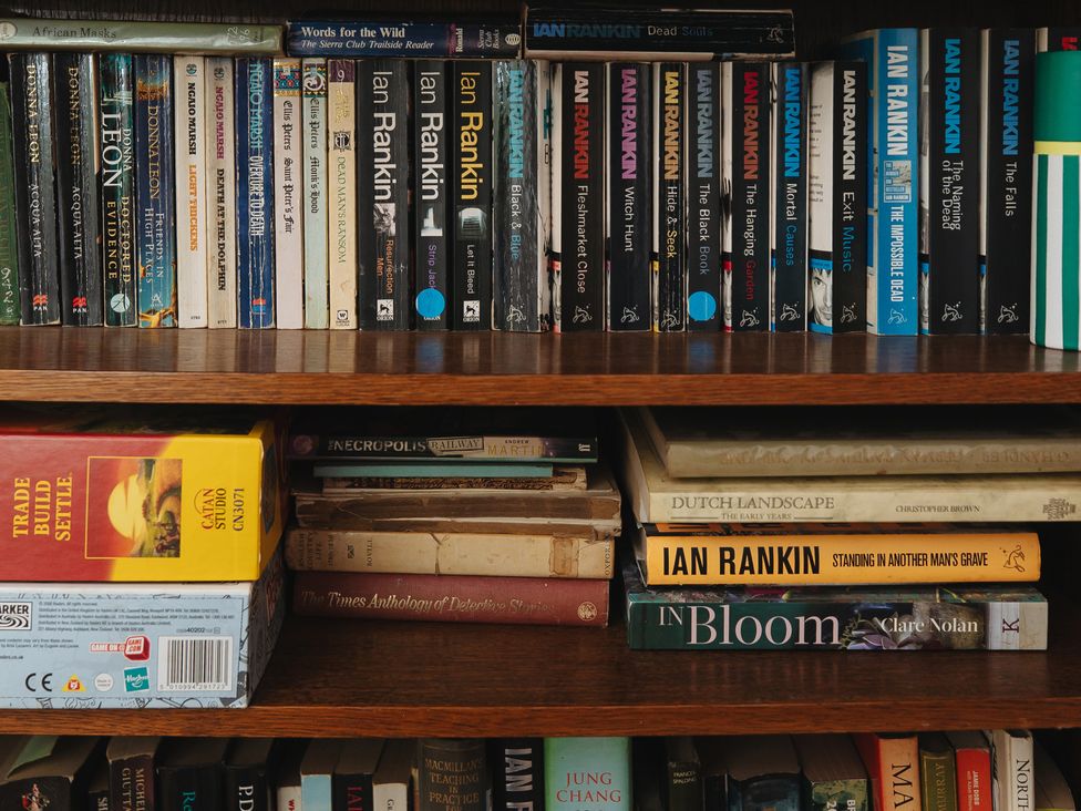 A bookshelf filled with various books and a board game at Cwmalis Hall, Llangollen