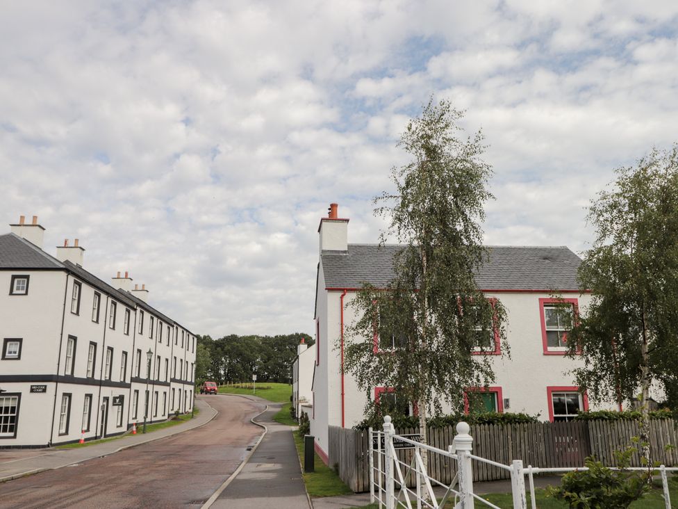 Houses along a road with trees and a fence at The Nook in Culloden