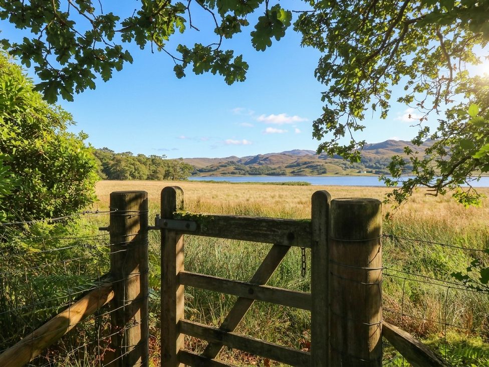 A view from a gate overlooking a field and lake at Clearwater House in Roshven near Glenuig