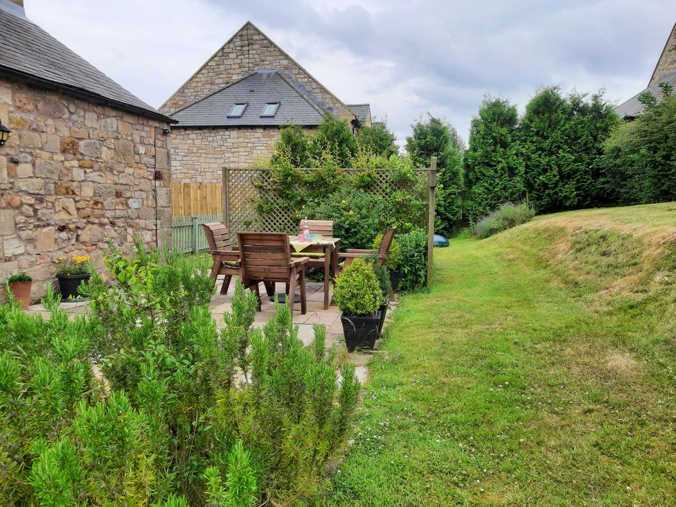 A garden with seating area and greenery at Hemmel Cottage in Chatton