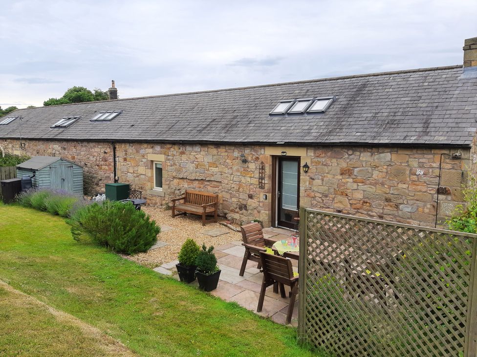 An outdoor area with a stone wall and seating at Hemmel Cottage in Chatton