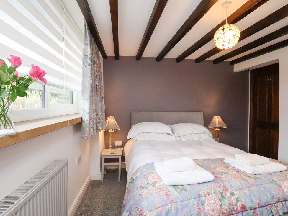 A bedroom with a bed, lamp, nightstand and flowers at Mill House in Robin Hood's Bay