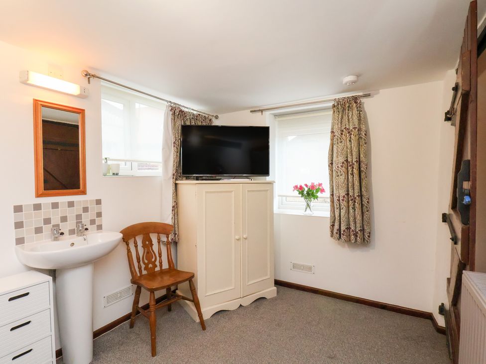 A bedroom with a TV, mirror, sink, chair, and cupboard at Stable Cottage in Robin Hoods Bay