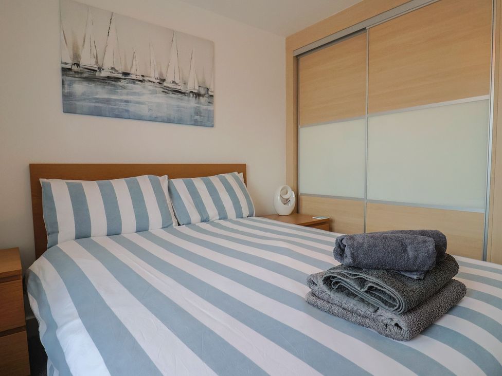 A bedroom with striped bedding and towels stacked at Harbourwalk in West Bay
