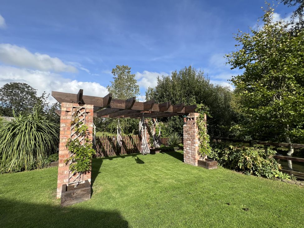 A garden with a pergola and hanging chairs at Moor End Manor in Stalmine