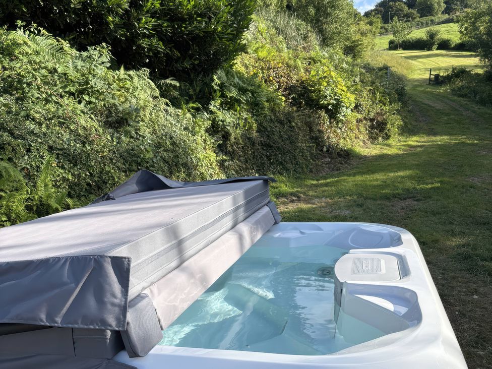 A hot tub with water and cover in an outdoor area at Lower Norton Farmhouse in Dartmouth