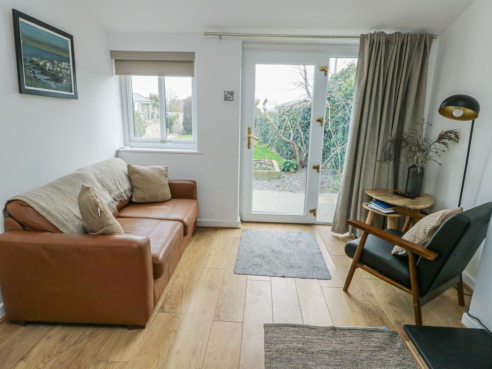 A living room with a sofa and door leading to the garden at Bwthyn in Moelfre