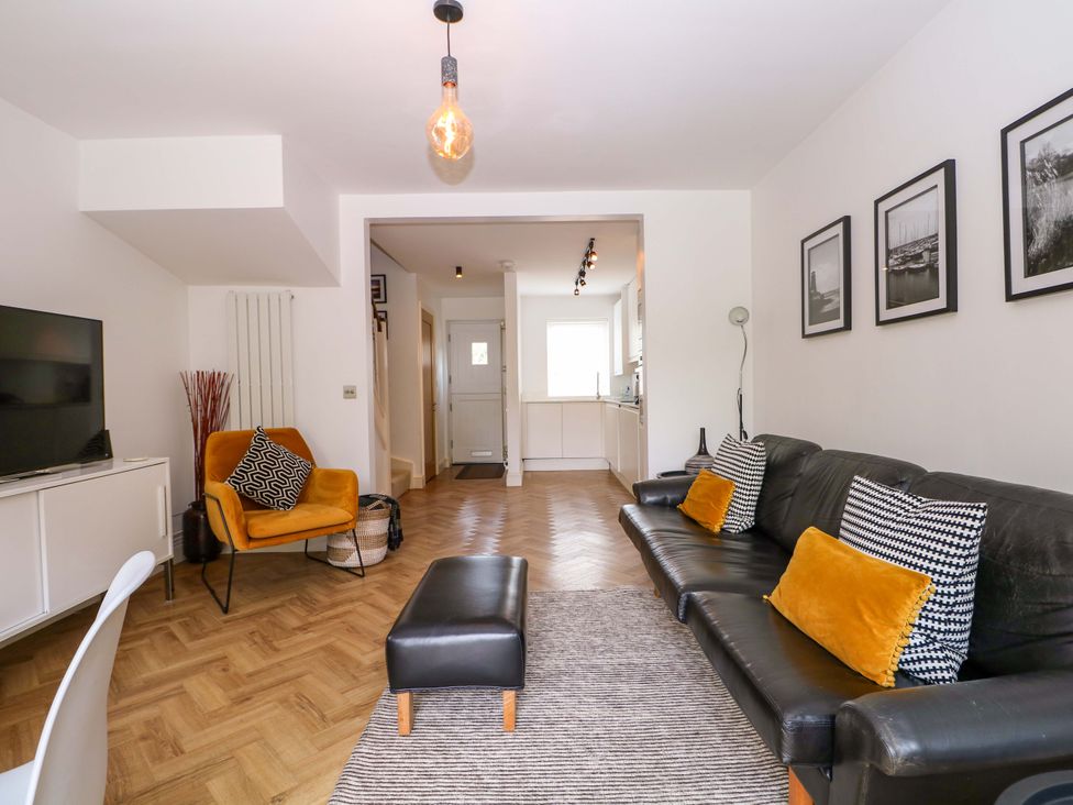 A living room with a television, sofa, armchair, and kitchen area at 2A The Mews Langstone
