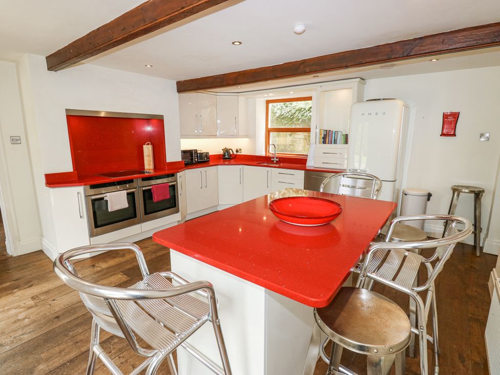 A kitchen with a red counter and stools at Woodbottom Farm in Meltham