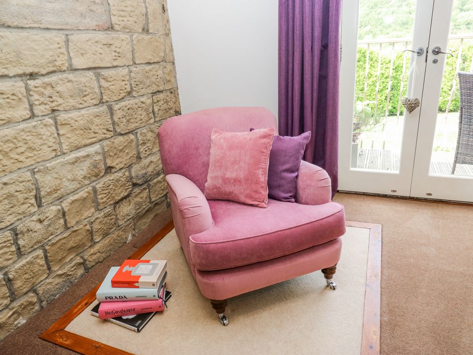 A pink chair with cushions and books in a living room at Woodbottom Farm Meltham