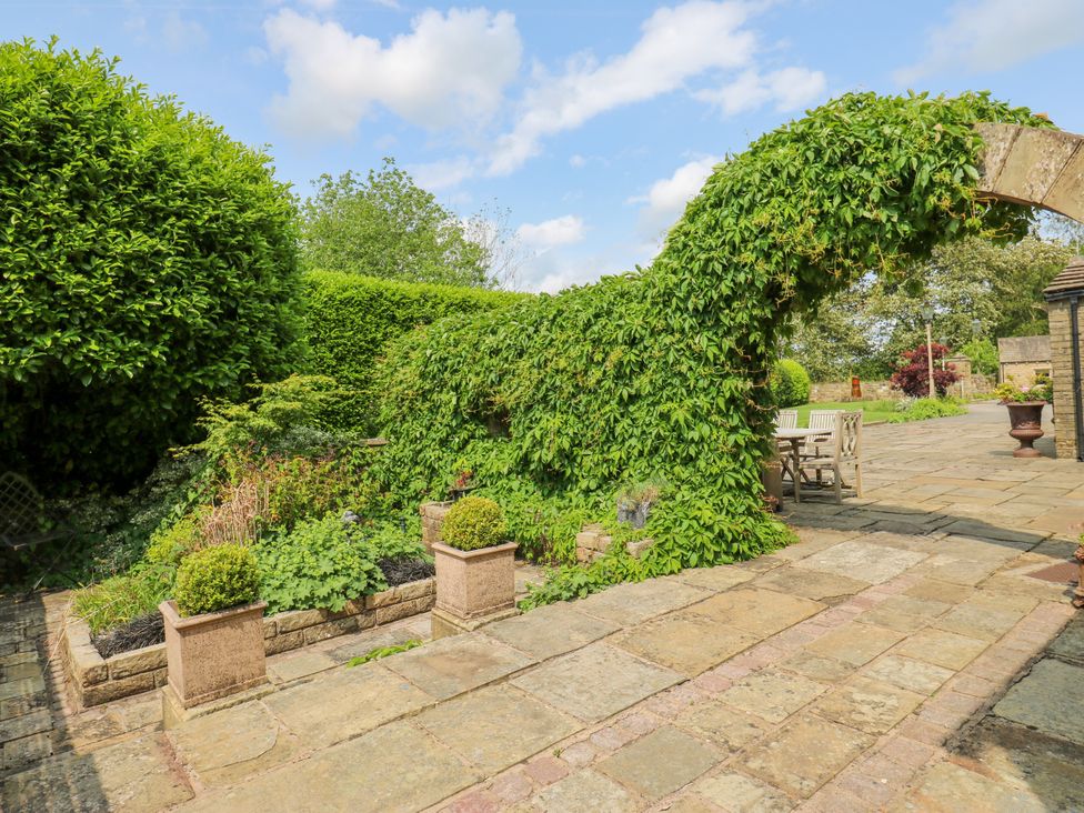 A garden with hedges and a patio seating area at Woodbottom Farm in Meltham