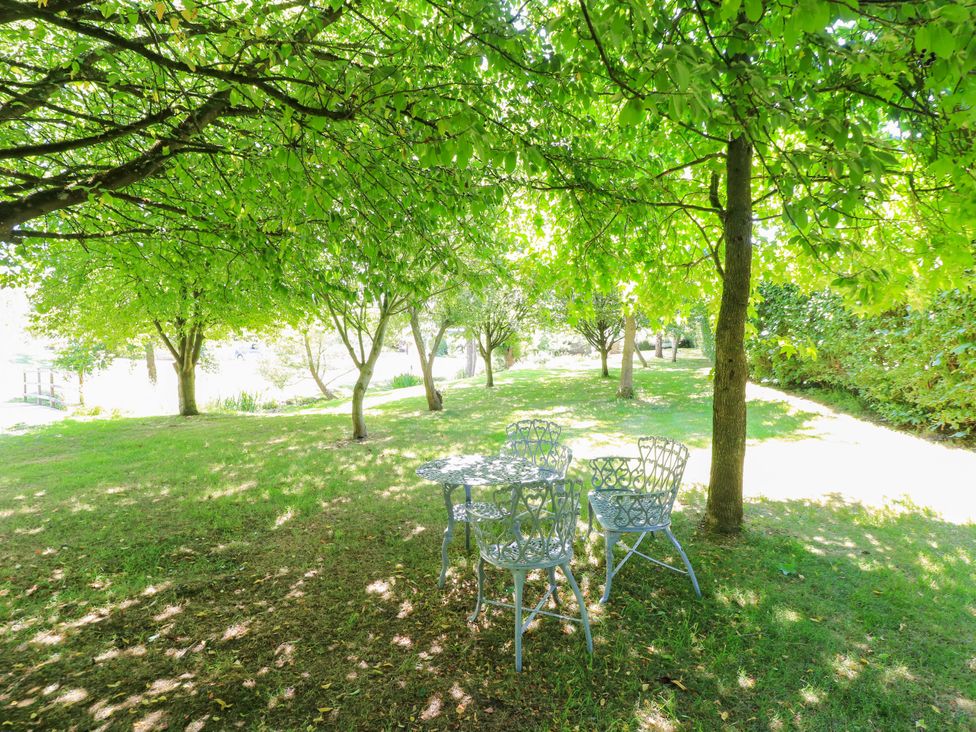 A table and chairs under trees in a garden at Pheasant Cottage in Priston Village, BATH