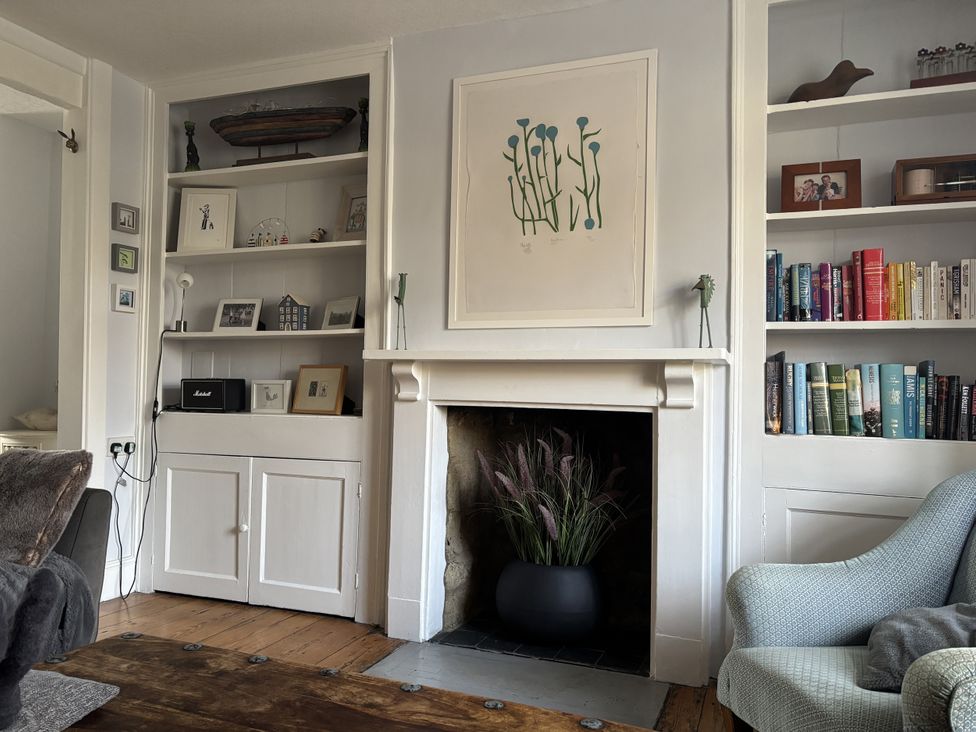 A living room with a bookshelf, fireplace, and armchair at Brock Cottage West Bay