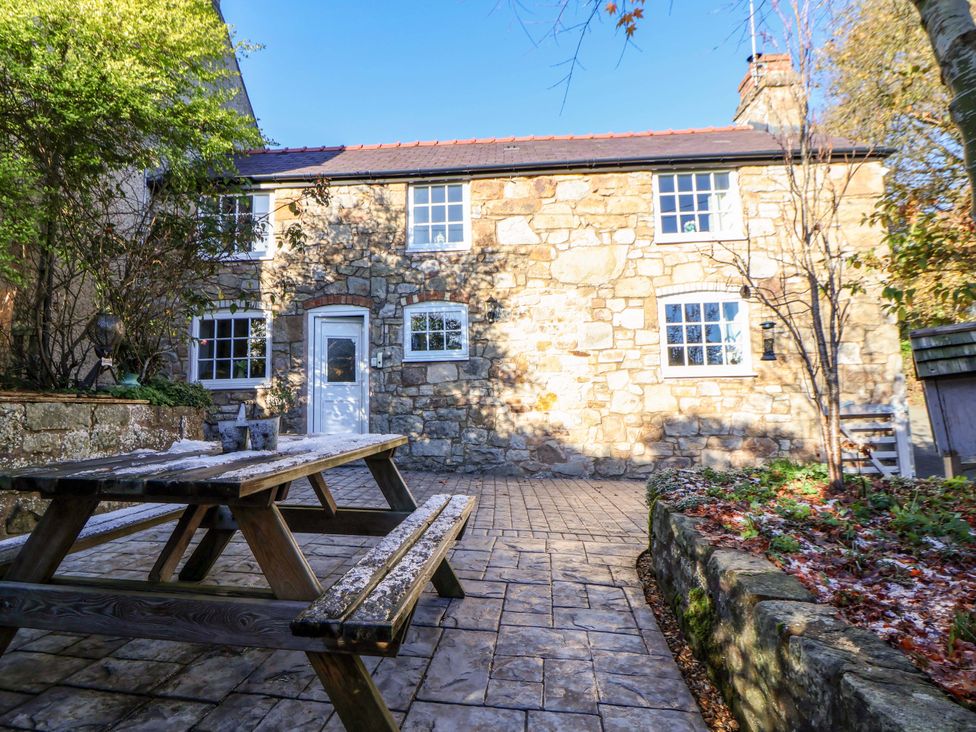 A stone house with a patio table and garden at Woodland Cottage in Garth