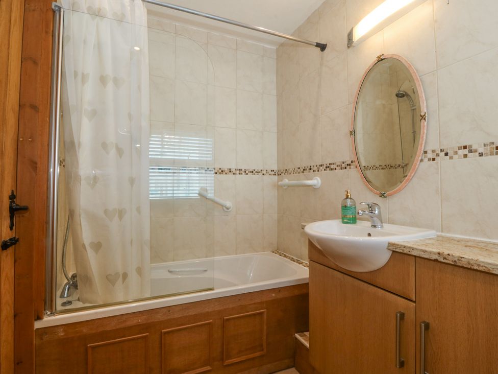 A bathroom with a bathtub shower combination a sink with a cabinet and an oval mirror at Bay View Apartment in Porthmadog