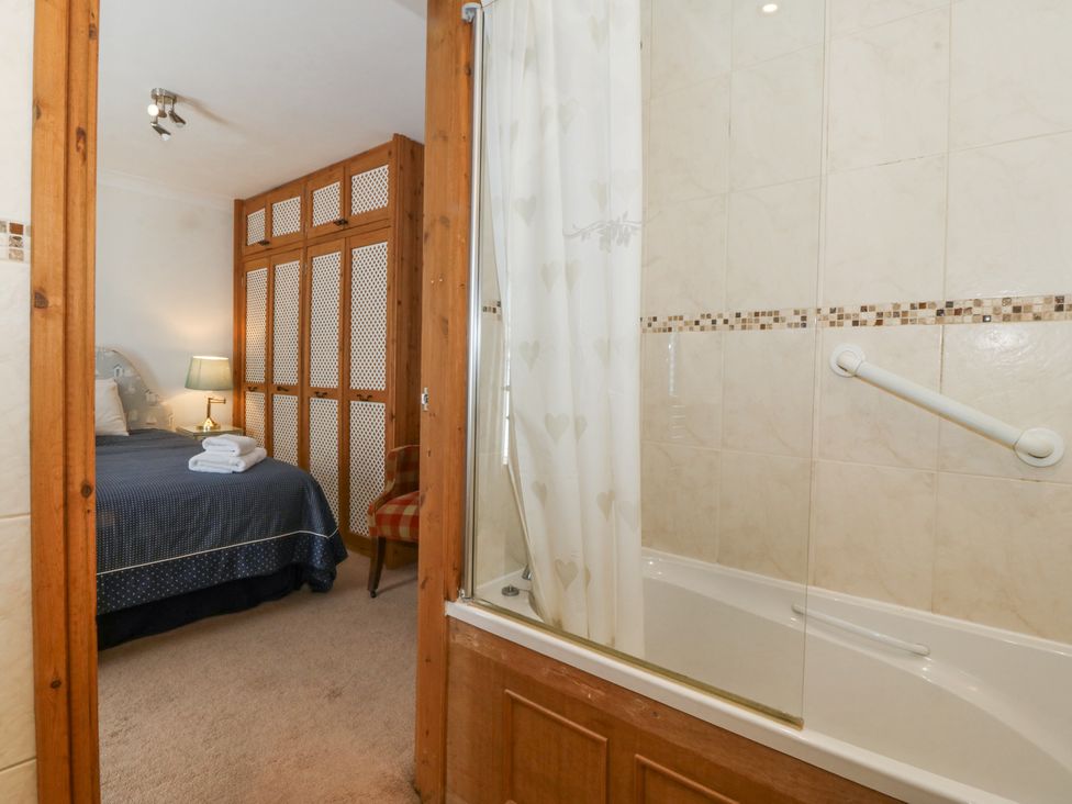 A bathroom with a bathtub and shower curtain next to a bedroom with a bed lamp and wardrobe at Bay View Apartment in Porthmadog
