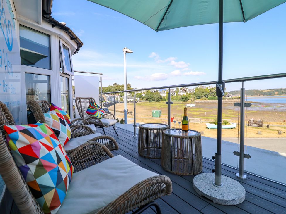 A balcony with chairs and tables overlooking the water at Bay View Apartment in Porthmadog