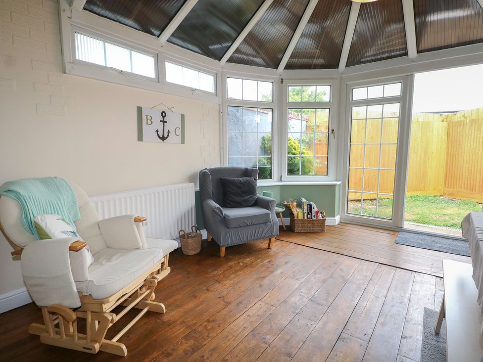 A conservatory with seating and a door leading to the garden at Bay Cosy in Pevensey Bay
