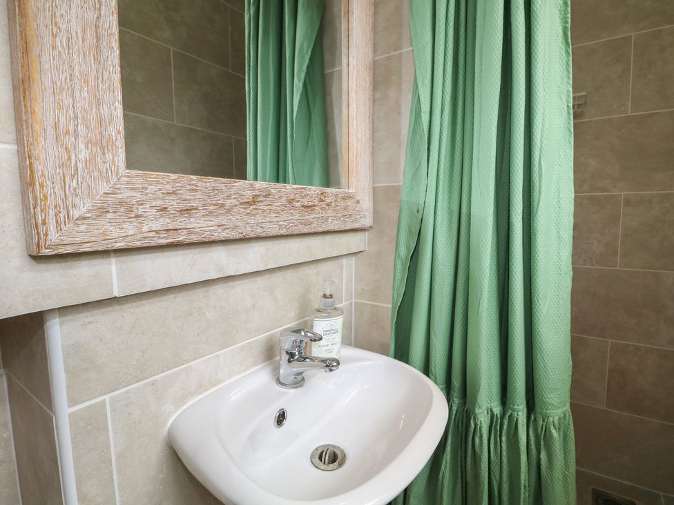 A bathroom with a sink, mirror, and green shower curtain at Bay Cosy Pevensey Bay