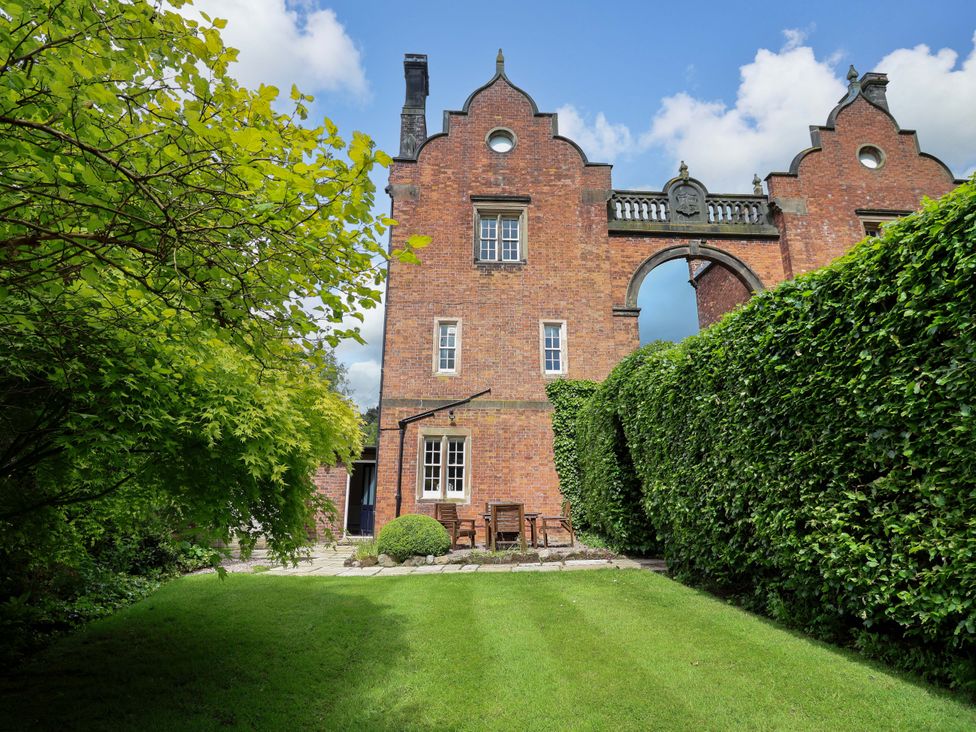 A garden with a brick building and furniture at South Tower Cottage in Capesthorne near Macclesfield