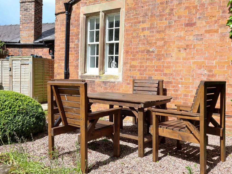 A table and chairs on gravel next to a brick wall at South Tower Cottage in Capesthorne near Macclesfield