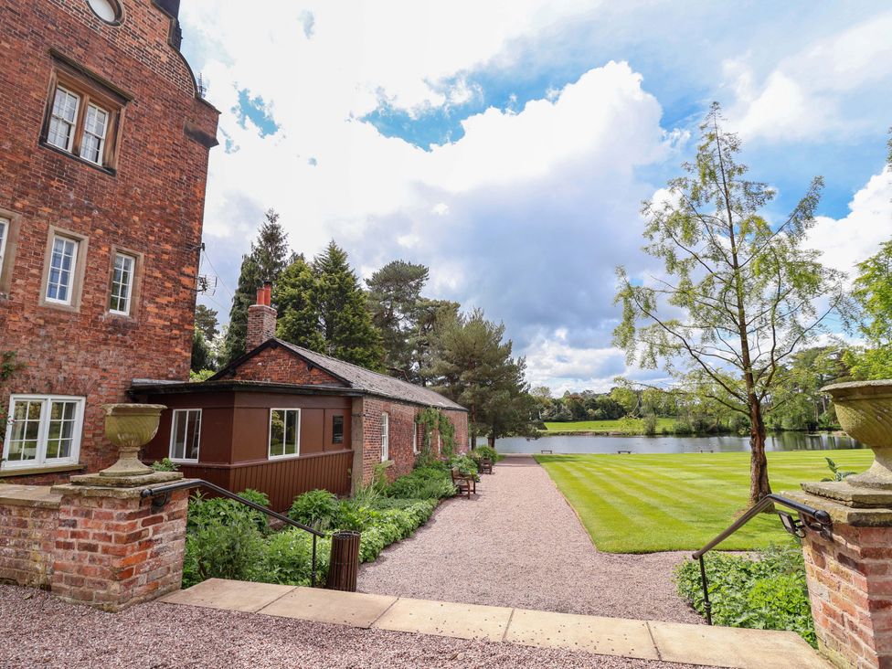 A garden area with a lake and brick buildings at South Tower Cottage Capesthorne near Macclesfield