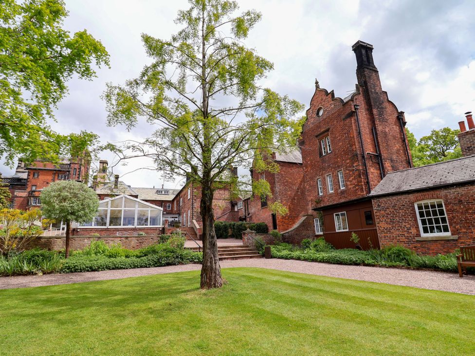A garden with a tree and brick buildings at South Tower Cottage Capesthorne near Macclesfield