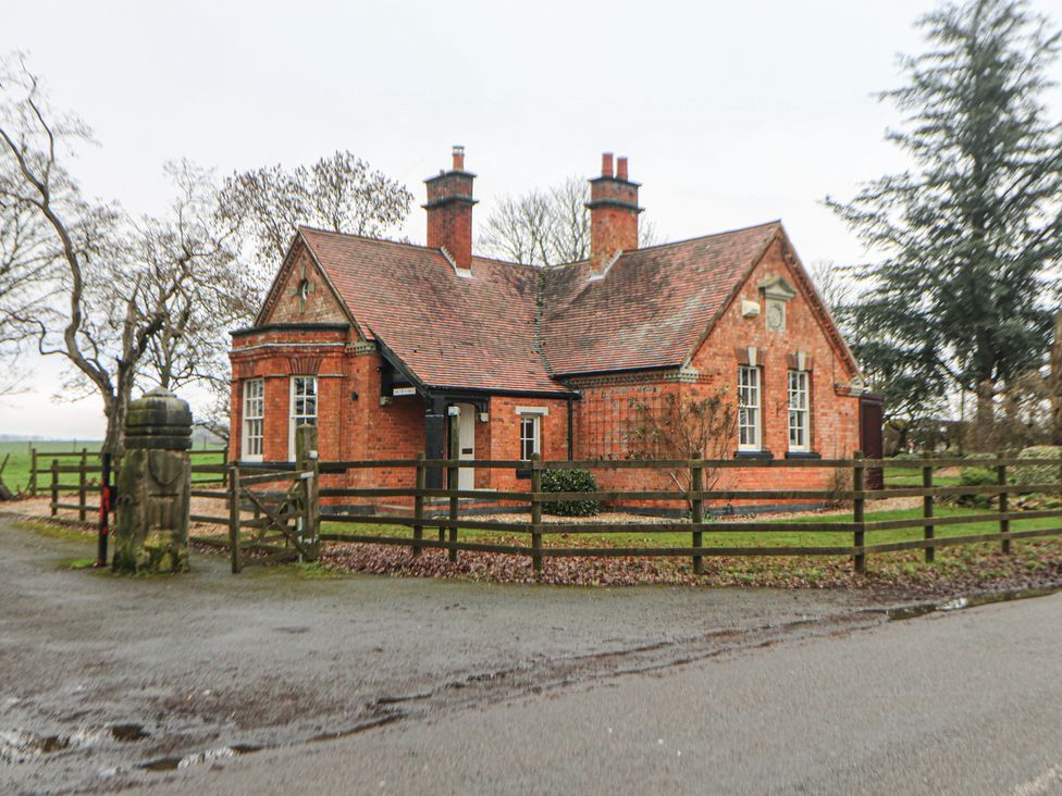 A brick house with a fence and trees at South Lodge - Longford Hall Farm Holiday Cottages Longford near Ashbourne