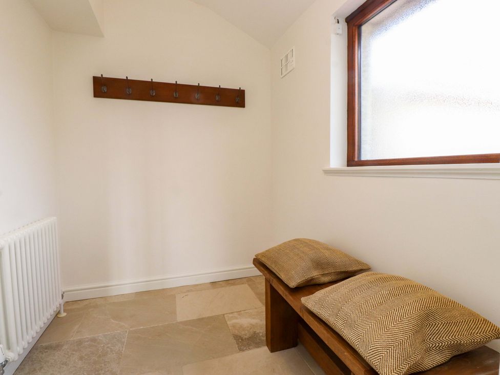 A hallway with coat hooks, a bench, and a radiator at Bryn Deryn in Criccieth