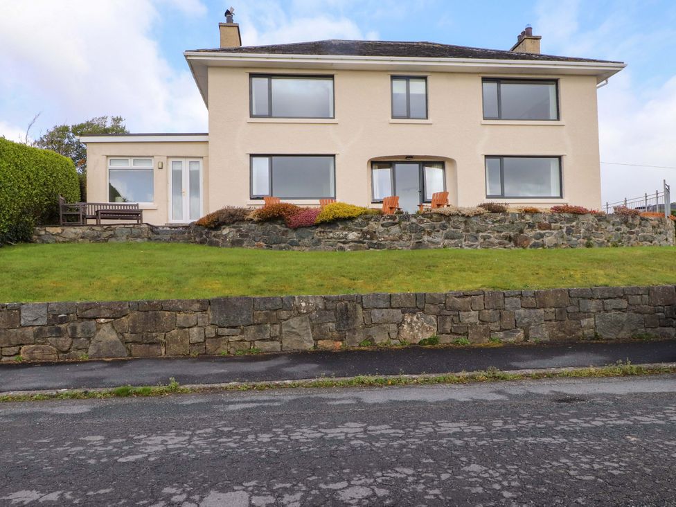 A house with a stone wall and lawn at Bryn Deryn in Criccieth