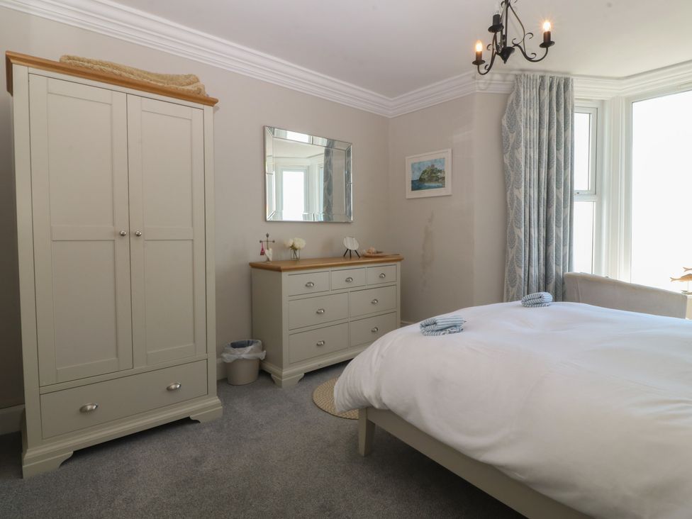 A bedroom with a bed, wardrobe, dresser, and mirror at Captain's Rest in Criccieth