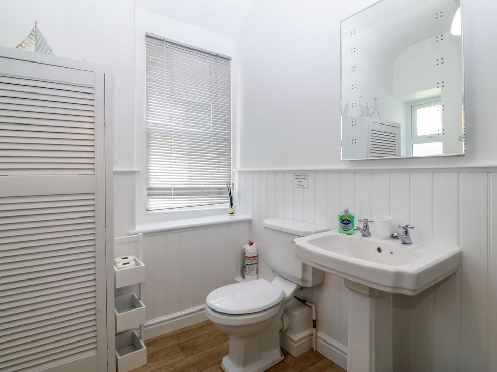 A bathroom with a sink, toilet, and mirror at Captain's Rest in Criccieth