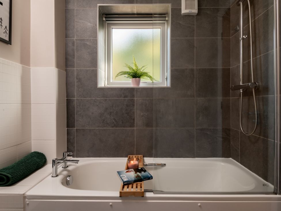 A bathtub with a shower and window at Coed y Felin in Conwy