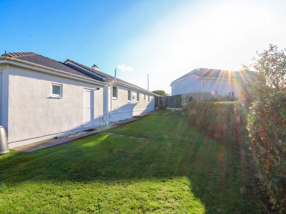 A side view of a house with grass and a fence at Curragho in Trearddur Bay