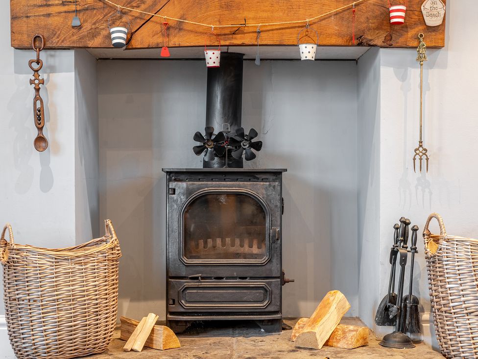 A living room with a wood stove and baskets at Curragho in Trearddur Bay