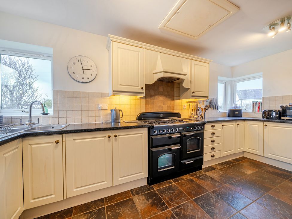 A kitchen with cabinets, stove, clock, and sink at Curragho in Trearddur Bay