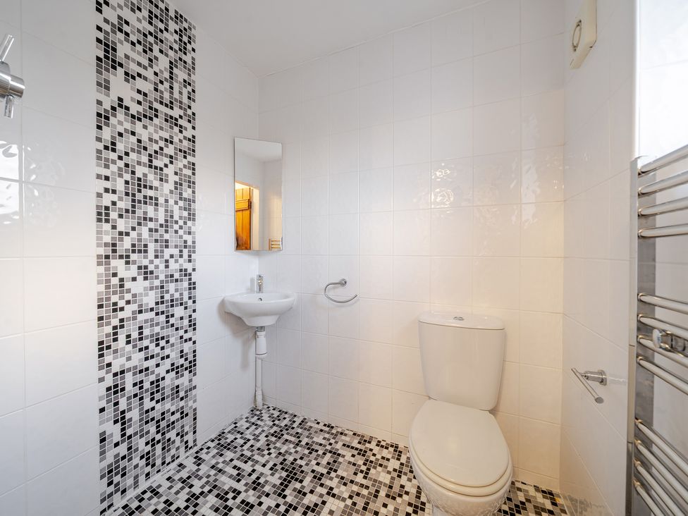 A bathroom with a toilet, hand basin, and mosaic tile wall at Curragho, Trearddur Bay