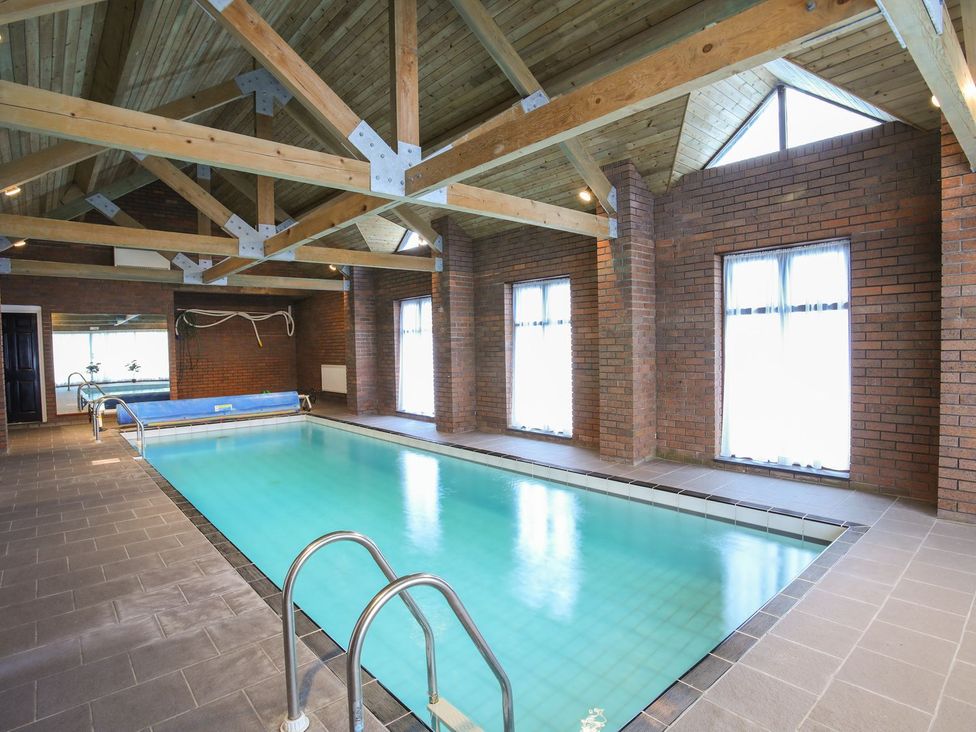 An indoor swimming pool with windows and wooden beams at Bryn Eira Tack Room in Llanfair PG
