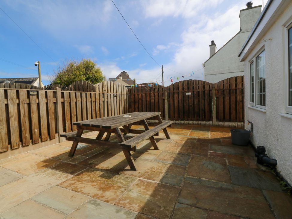 An outdoor patio with a wooden table and fence at Farm Cottage in Cemaes Bay
