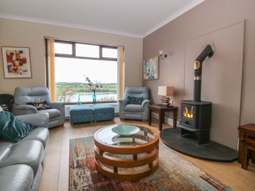 A living room with a wood stove and large windows at Gwylan Uchaf in Y Felinheli